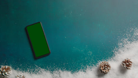 Overhead-Shot-Of-Person-With-Green-Screen-Mobile-Phone-Above-Christmas-Background